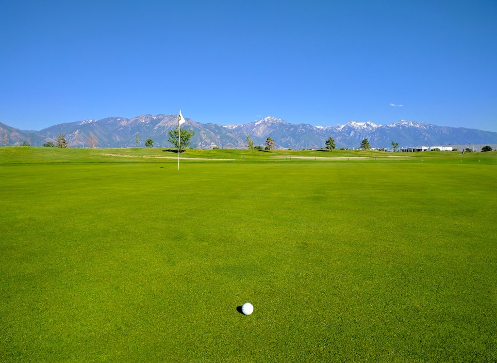 View of golf course green with mountains in distance